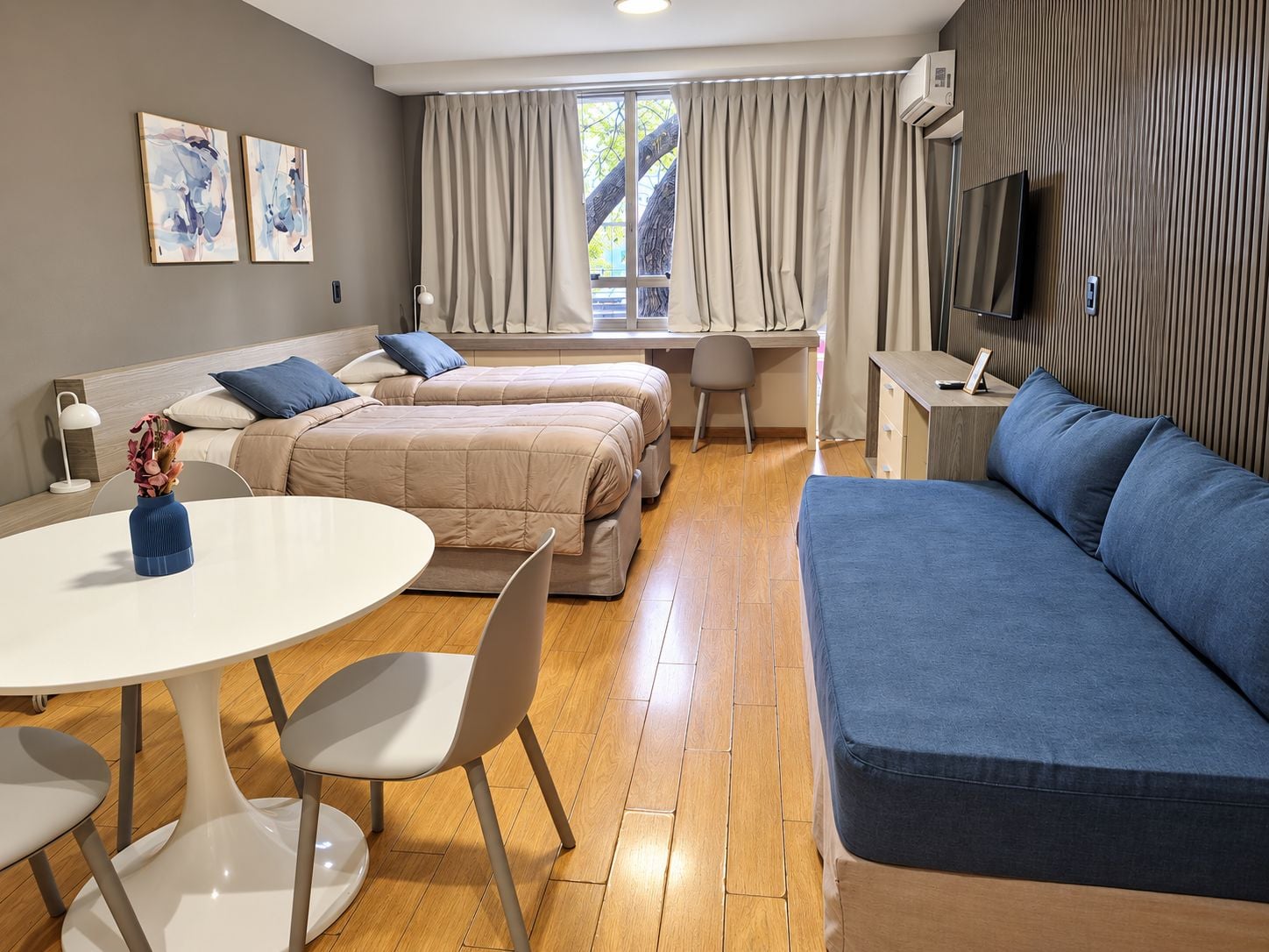 Ein modernes Hotelzimmer mit einer Couch, zwei Betten, einem Schreibtisch und einem Fernseher.