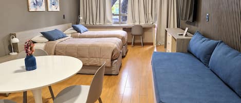 A modern hotel room with a sofa, two beds, a desk, and a TV.