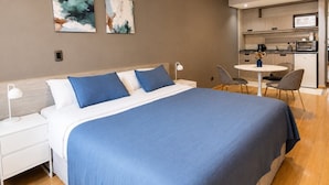 A modern bedroom with a large bed, a bedside table, a desk, and a kitchenette. - Ayres Apartments Recoleta - Uriburu (Buenos Aires)