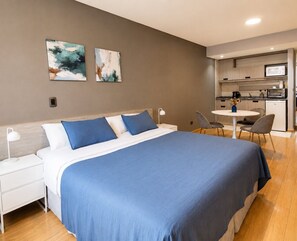 Une chambre moderne avec un grand lit, une table de chevet, un bureau et un coin cuisine.