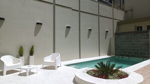 A pool area with a white pool, two white chairs, a small table, and a planter with red flowers. - Ayres Apartments Recoleta - Uriburu (Buenos Aires)