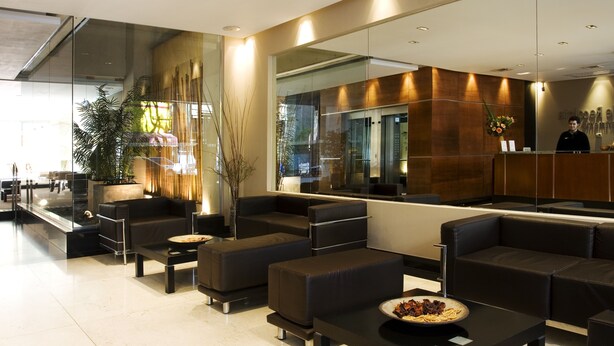 A modern lobby with black leather sofas, a reception desk, and a large mirror reflecting the interior. - Ayres Apartments Recoleta - Uriburu (Buenos Aires)