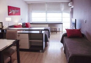 Una camera d'albergo con un letto, una scrivania, una sedia, una televisione e una finestra con tende.