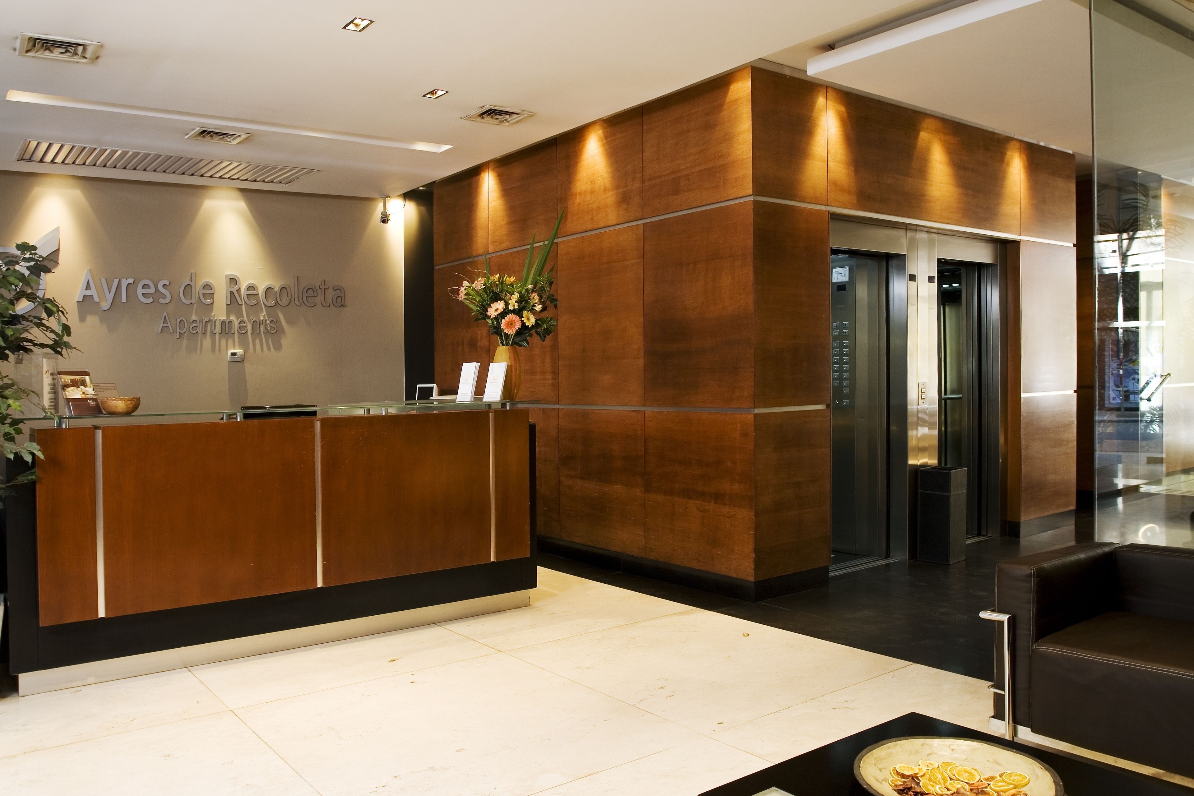 A reception desk with a wooden finish, a sign reading "Ayres de Recoleta Apartments," and a vase of flowers.