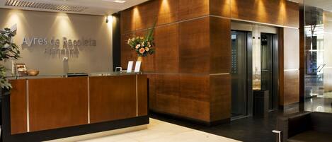 A reception desk with a wooden finish, a sign reading "Ayres de Recoleta Apartments," and a vase of flowers.