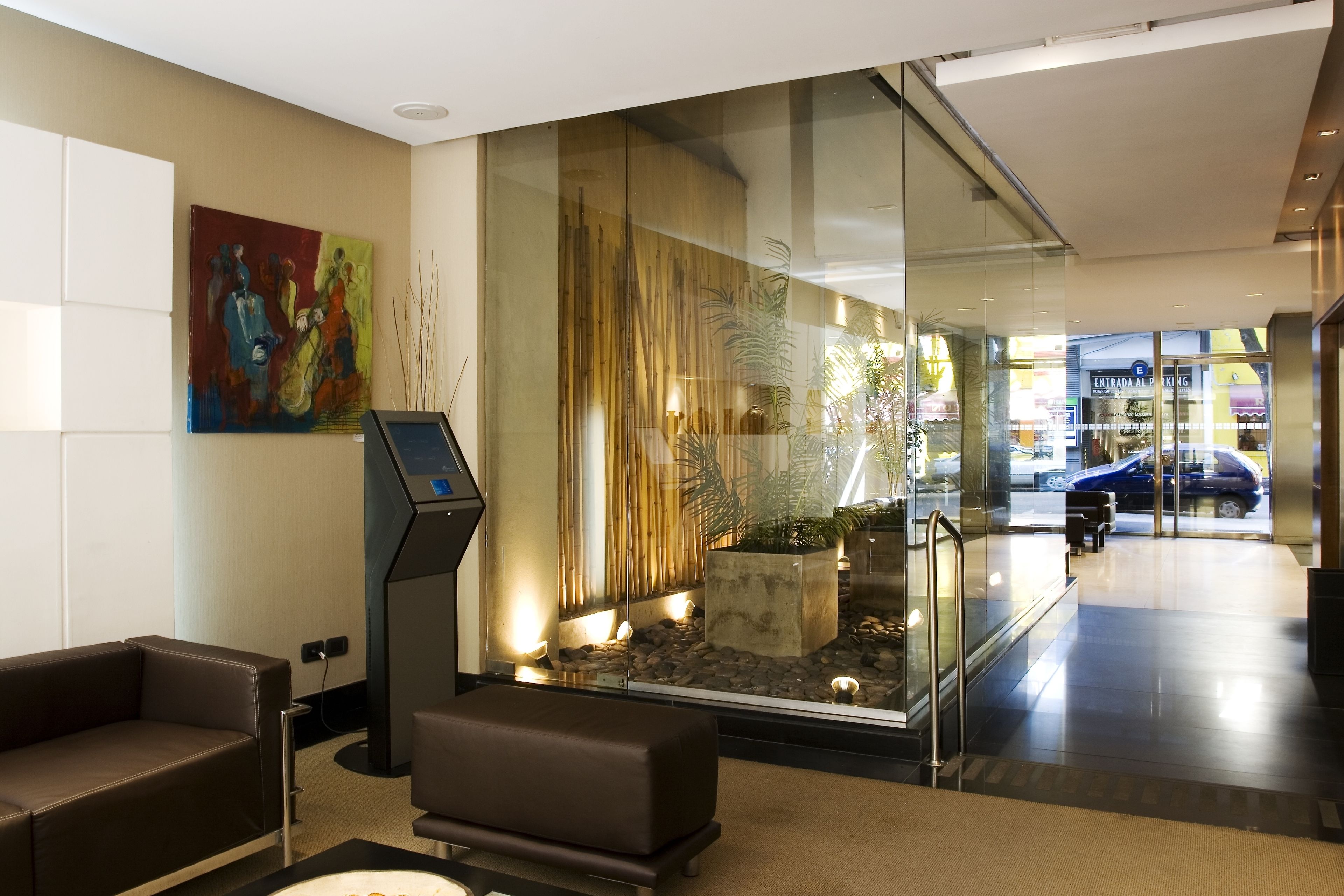 A modern lobby with a seating area, a digital kiosk, and a glass wall with a view of the street.