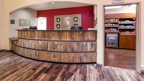 A reception area with a wooden reception desk, a red accent wall, and a kitchenette with shelves stocked with snacks.