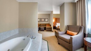 A hotel room with a large bathtub, a sofa, a chair, and a small table.
