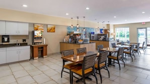 A modern kitchen with a microwave, coffee machine, and a juice dispenser. There is a dining area with wooden tables and chairs.
