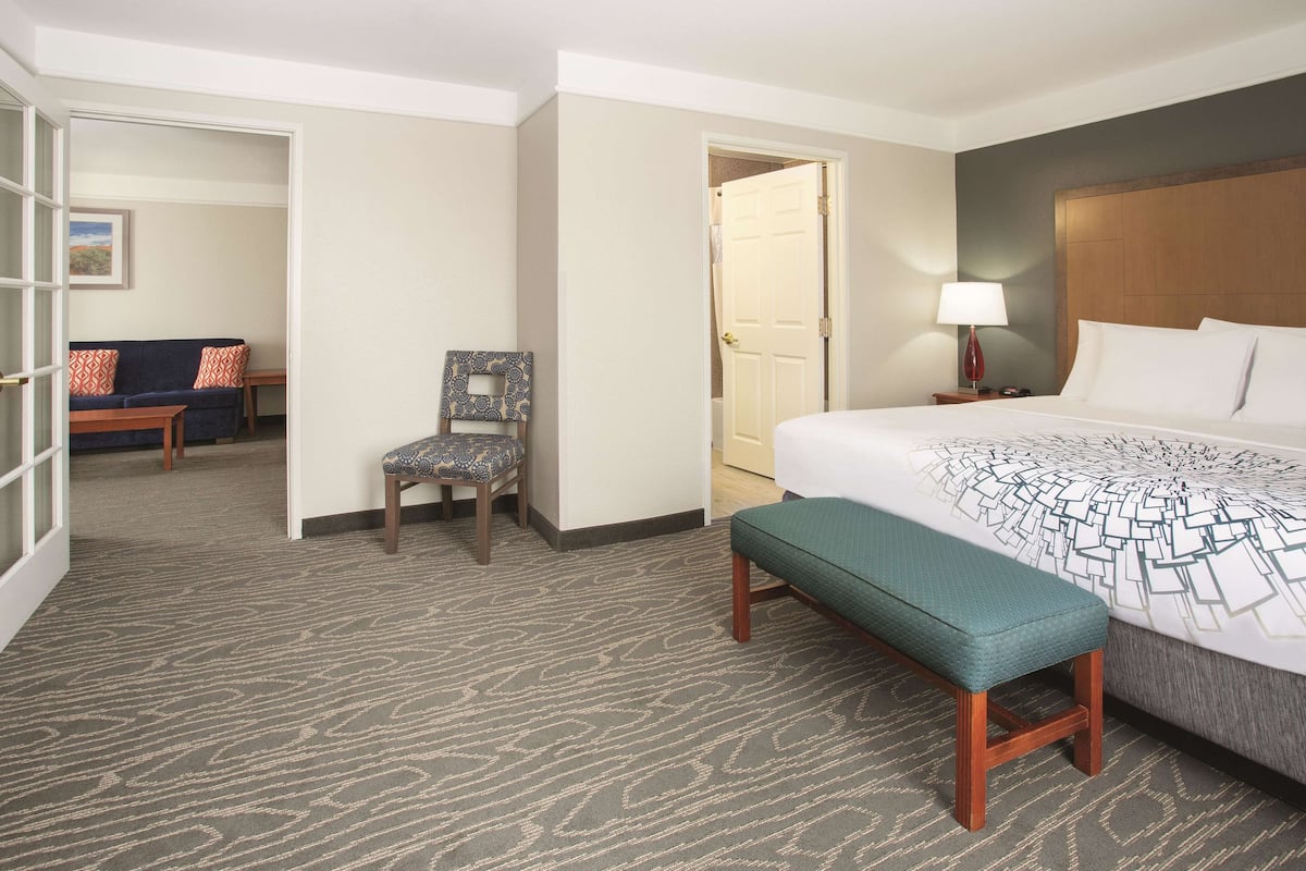 A hotel room with a large bed, a bench, a chair, a desk, and a door leading to another room.