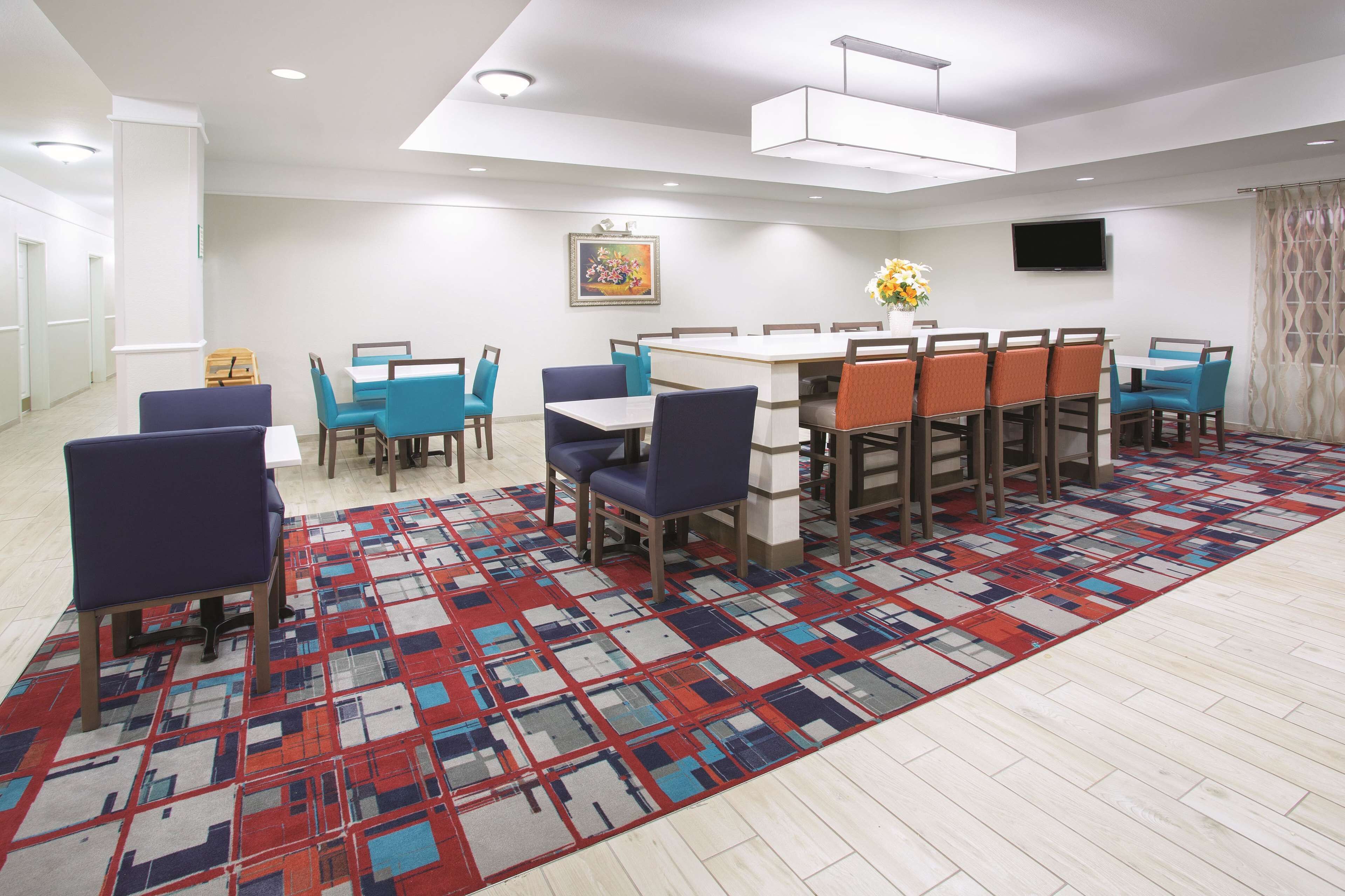 A modern dining area with a patterned rug, blue and orange chairs, and a white table.