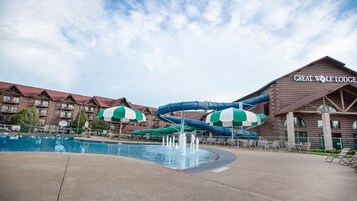 Un área de piscina con toboganes y sombrillas, un edificio de cabañas de madera y un cielo despejado.
