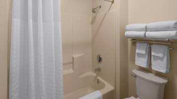 Een badkamer met een douche, een bad en een toilet. Handdoeken liggen op een rek.