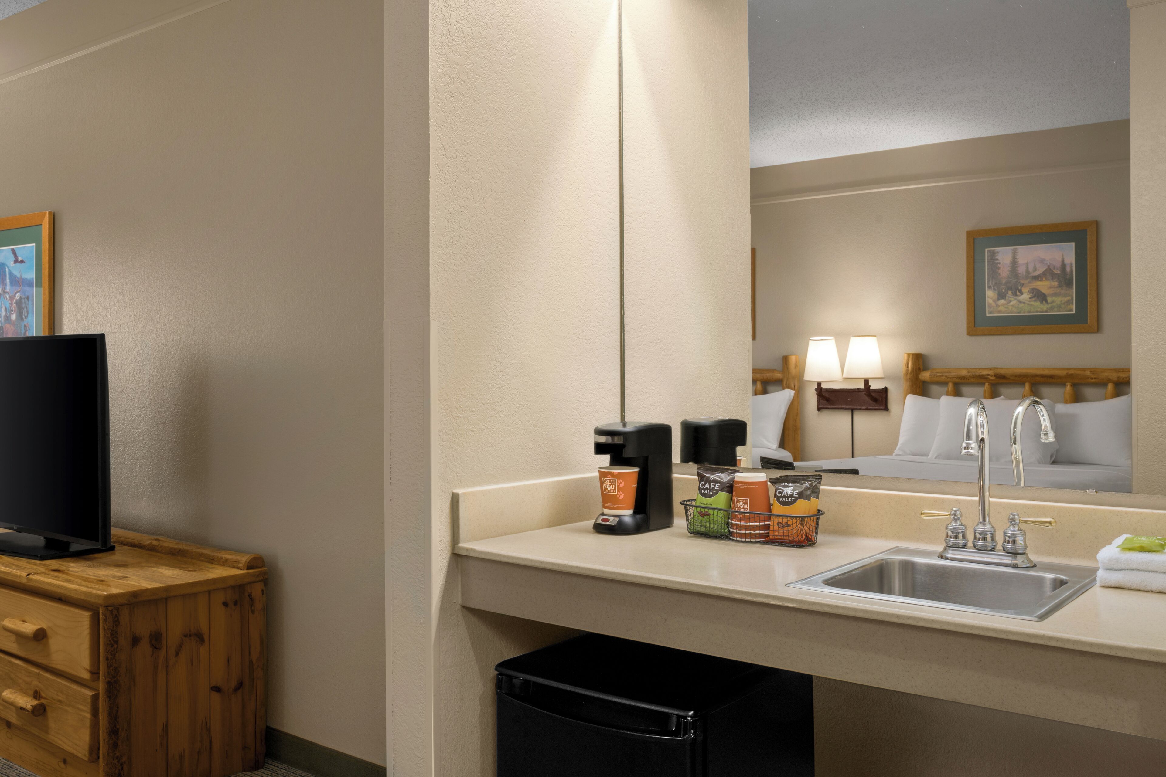 A hotel bathroom with a sink, mirror, and a television on a wooden cabinet.