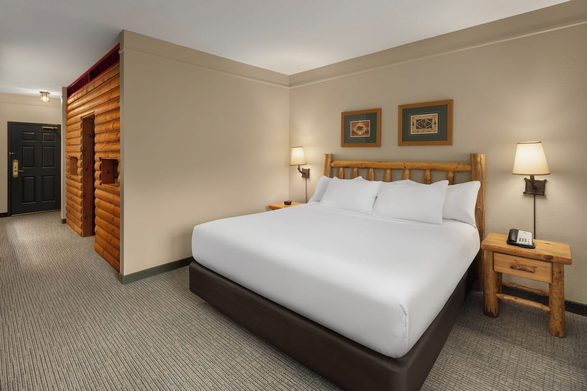 Habitación de hotel con una cama grande, cabecera de madera, dos lámparas de noche, un mesita de noche de madera y una puerta con marco rojo.