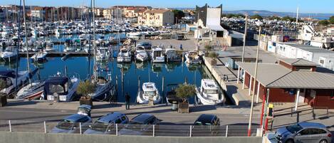 Un puerto deportivo con numerosos barcos amarrados, un área de estacionamiento con coches y edificios al fondo.