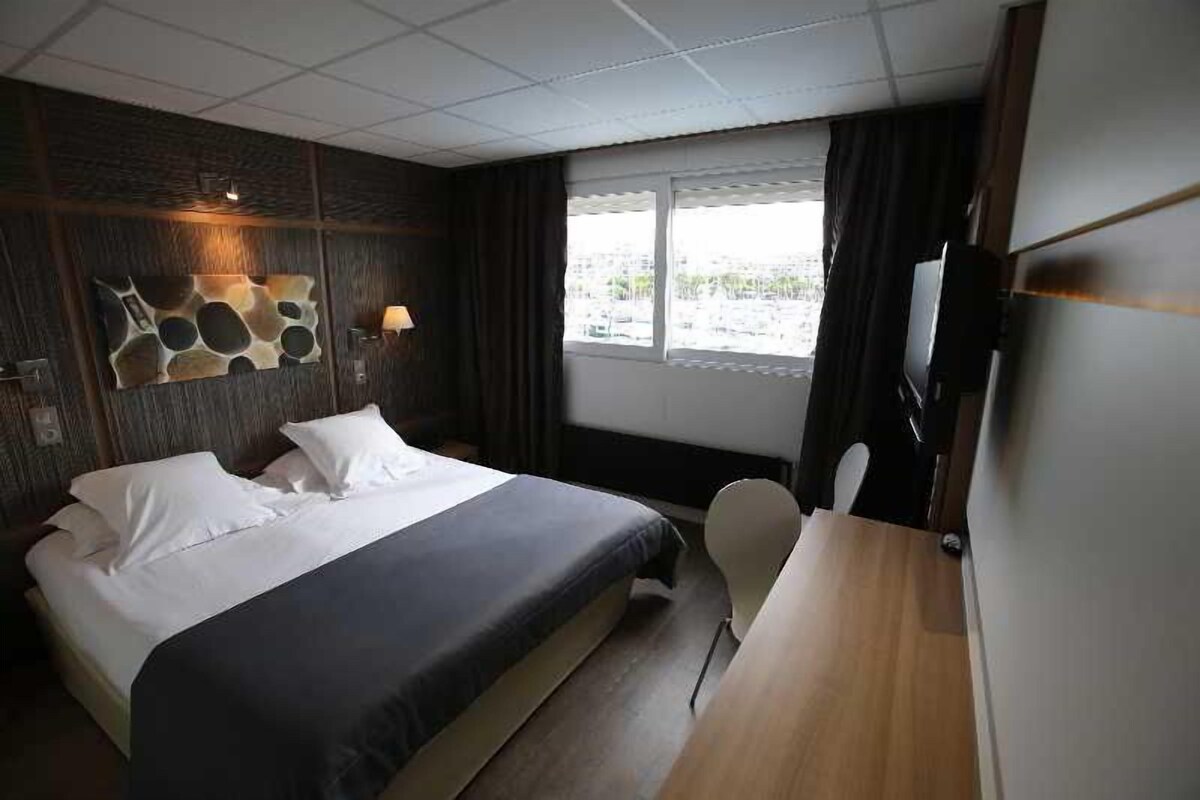 A hotel room with a bed, a desk, a chair, a TV, and a window with curtains.