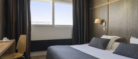 A hotel room with a large bed, a desk, a chair, and a window with curtains.