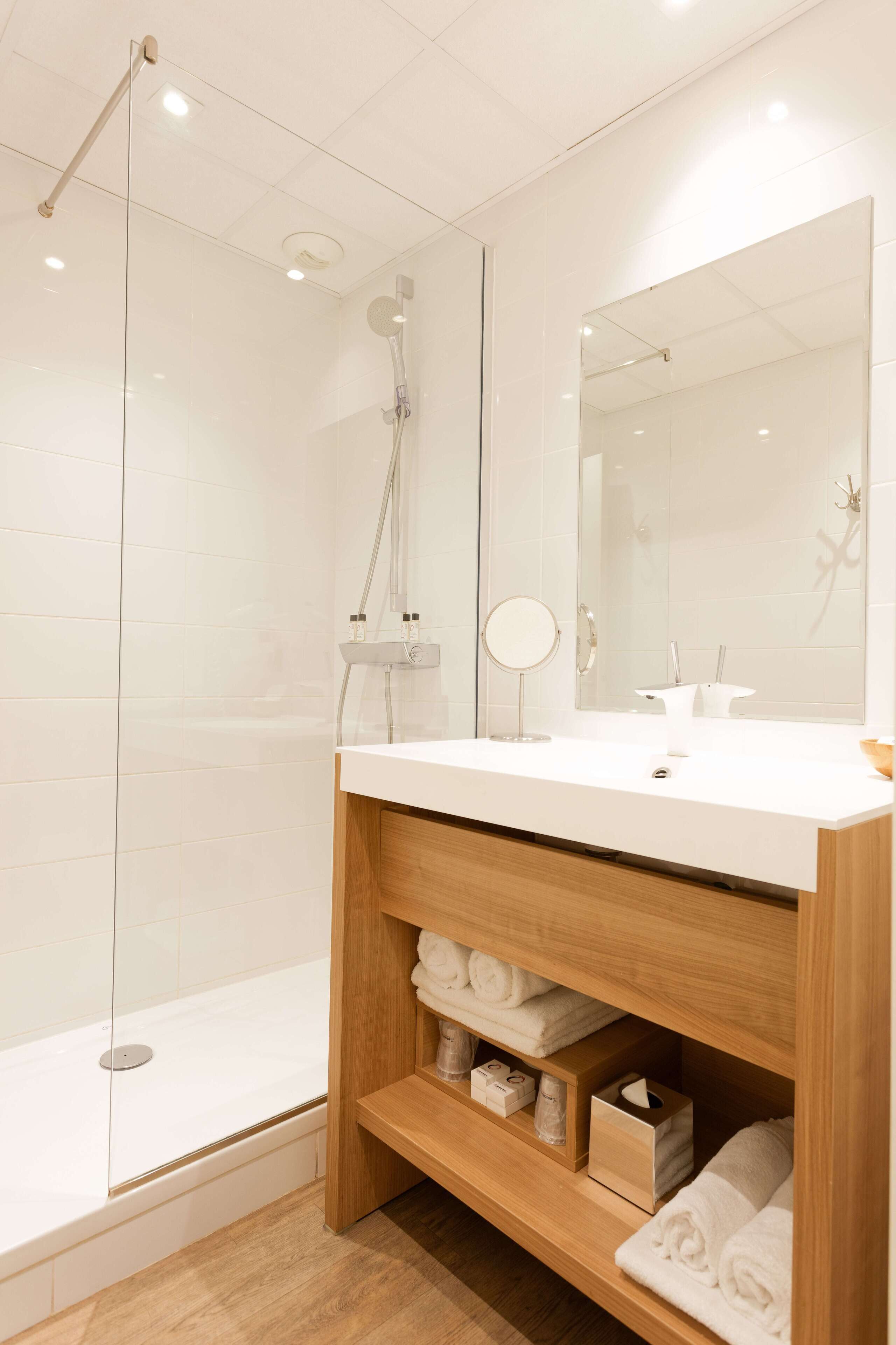 Une salle de bain moderne avec une douche à parois de verre, un meuble-lavabo en bois avec un miroir et des serviettes soigneusement pliées.