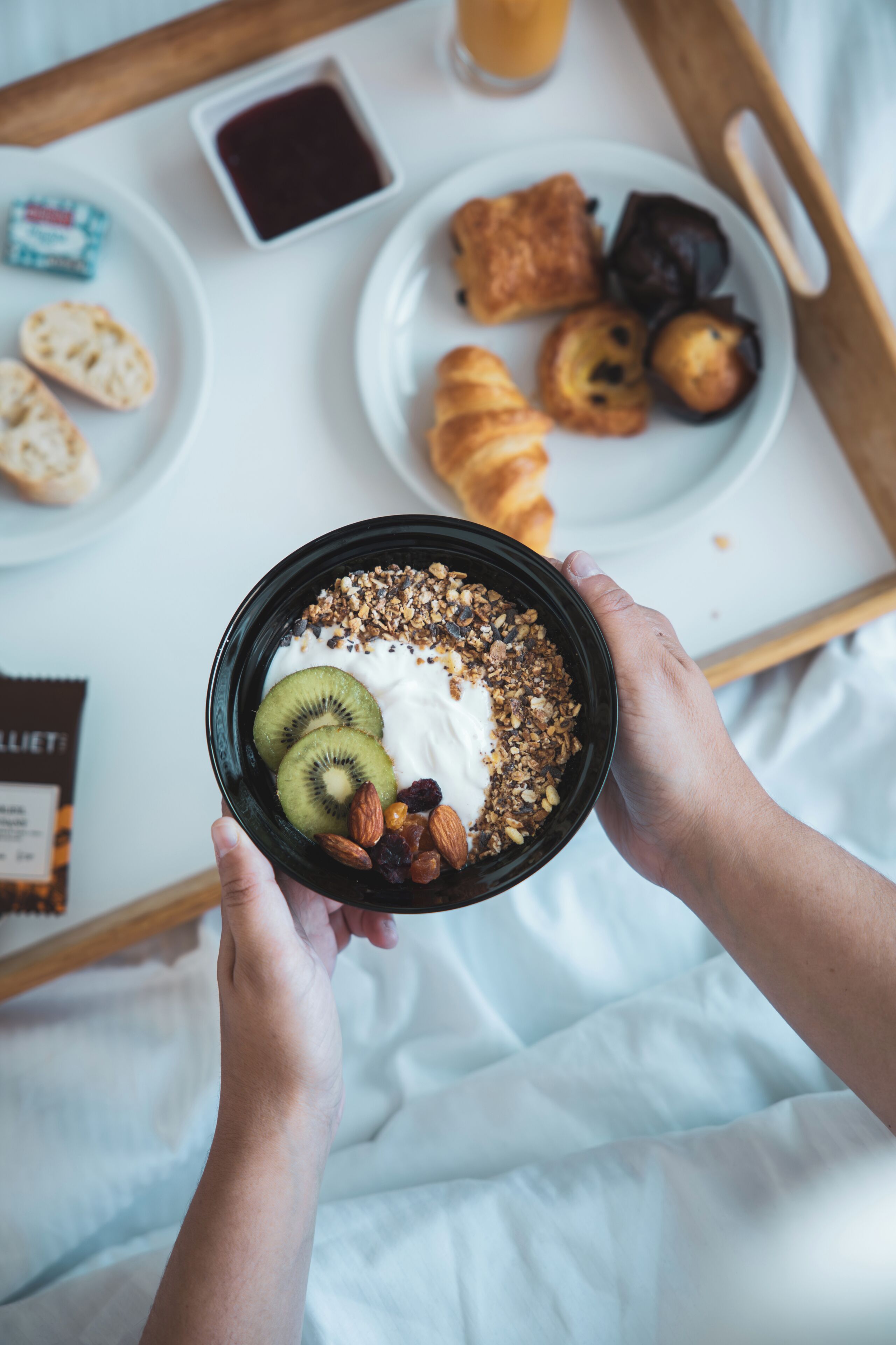 A breakfast tray with croissants, a bowl of yogurt with fruits and granola, and a packet of chocolate.