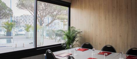Un salón de conferencias con un amplio ventanal, una mesa blanca y posavasos rojos.