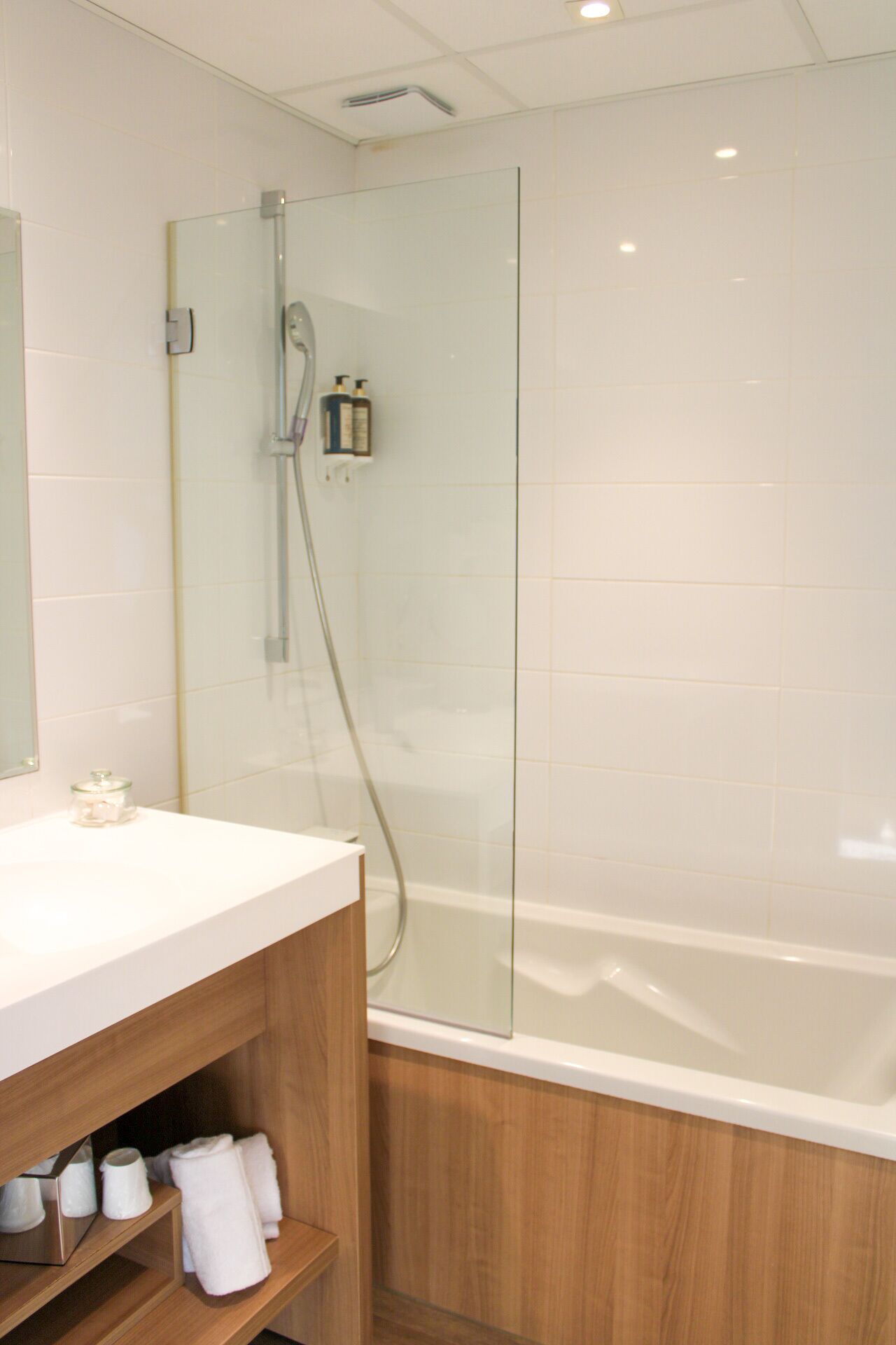 A modern bathroom with a glass-enclosed shower, a white bathtub, and a wooden vanity with towels.
