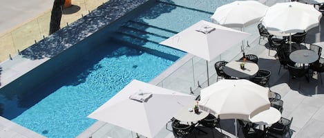A swimming pool with surrounding outdoor seating and umbrellas.