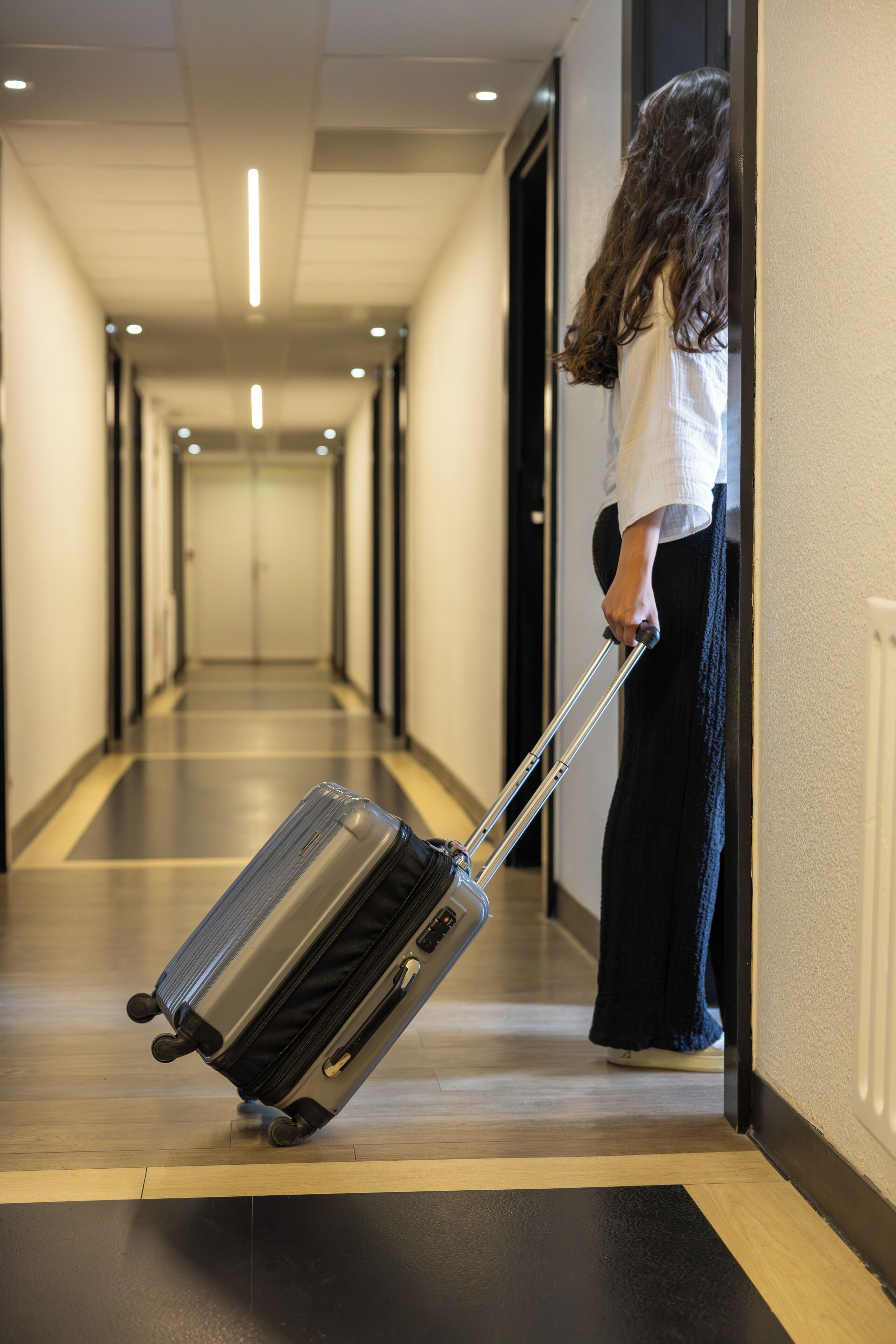 A hotel corridor with a person pulling a suitcase.