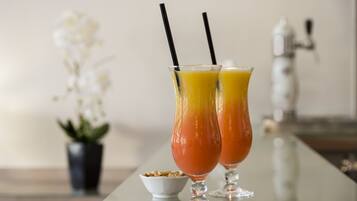 Deux verres de jus d’orange avec des pailles noires, posés sur une surface réfléchissante.