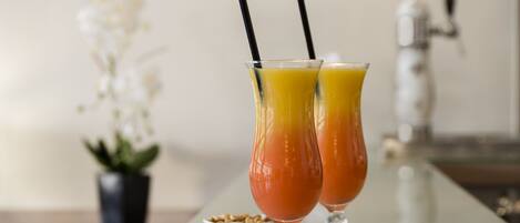 Two glasses of orange juice with black straws on a reflective surface.