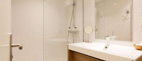 A modern bathroom with a glass shower enclosure, a wooden vanity with a mirror, and a white countertop.