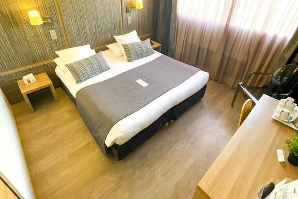 Una habitación de hotel con una cama grande, mesitas de noche, un escritorio y una silla.