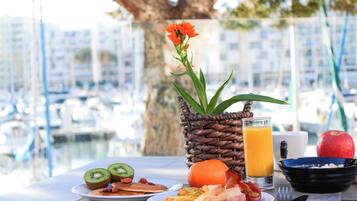 Una mesa de desayuno con platos de comida, un vaso de jugo de naranja y una cesta de mimbre con flores.