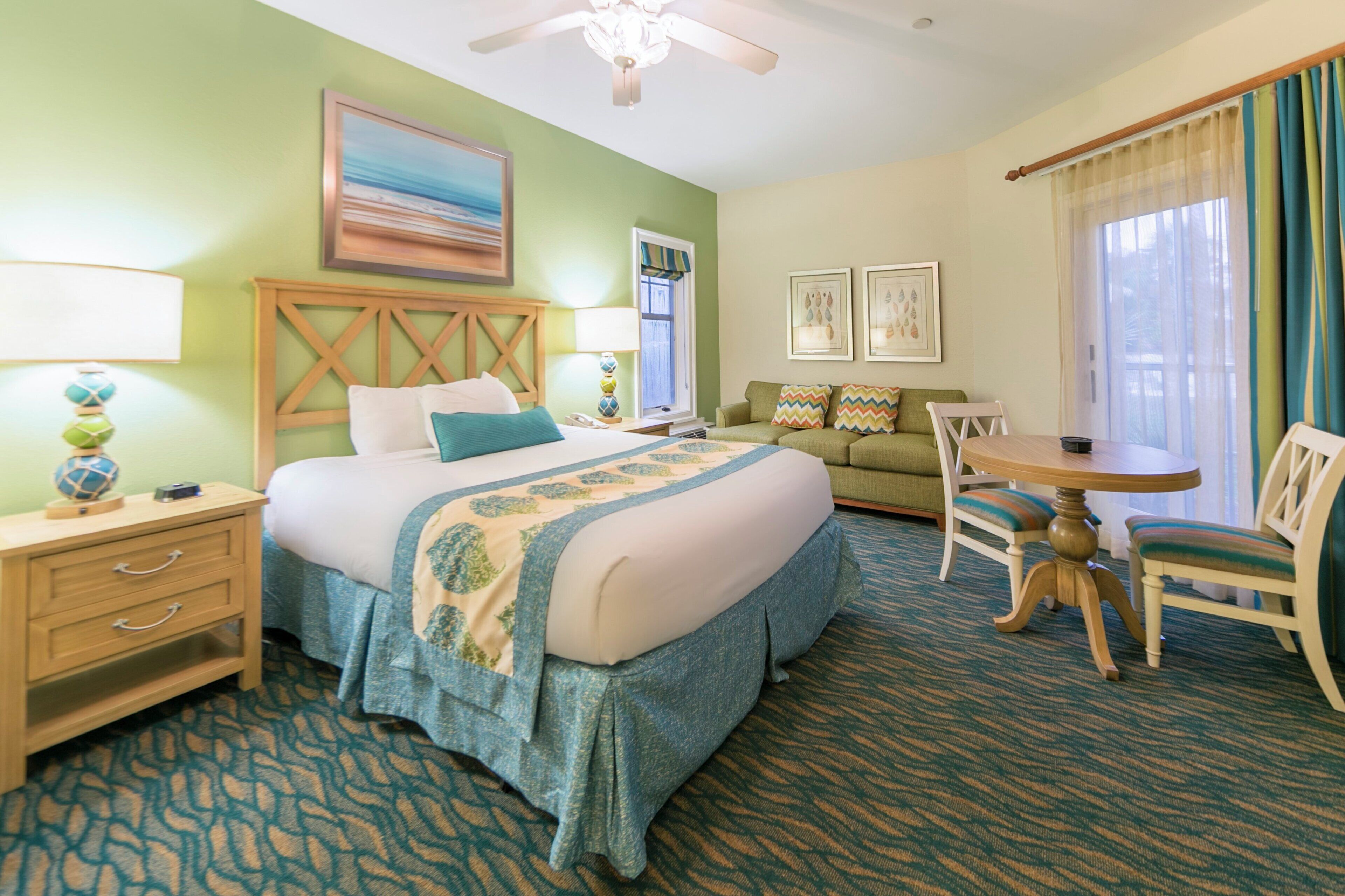 A hotel room with a bed, bedside table, lamp, and a view of the outdoors.