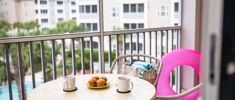 A balcony with a table set for two, a chair, and a pink cushion.