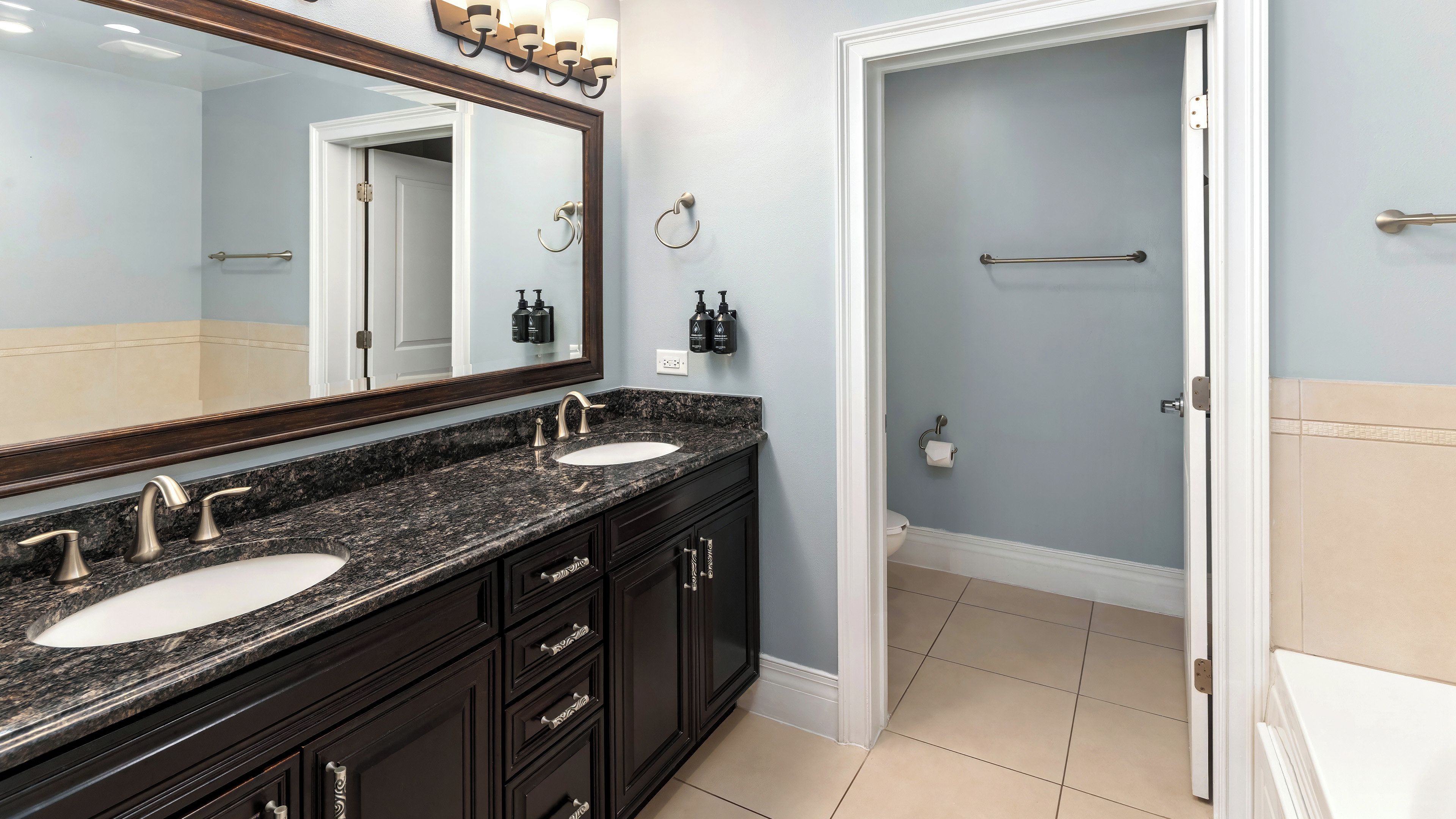 A bathroom with two sinks, a large mirror, and a door leading to a shower area.