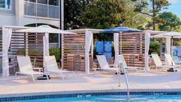 A poolside area with lounge chairs and umbrellas, a pool with a tiled edge, and a wooden pergola structure.
