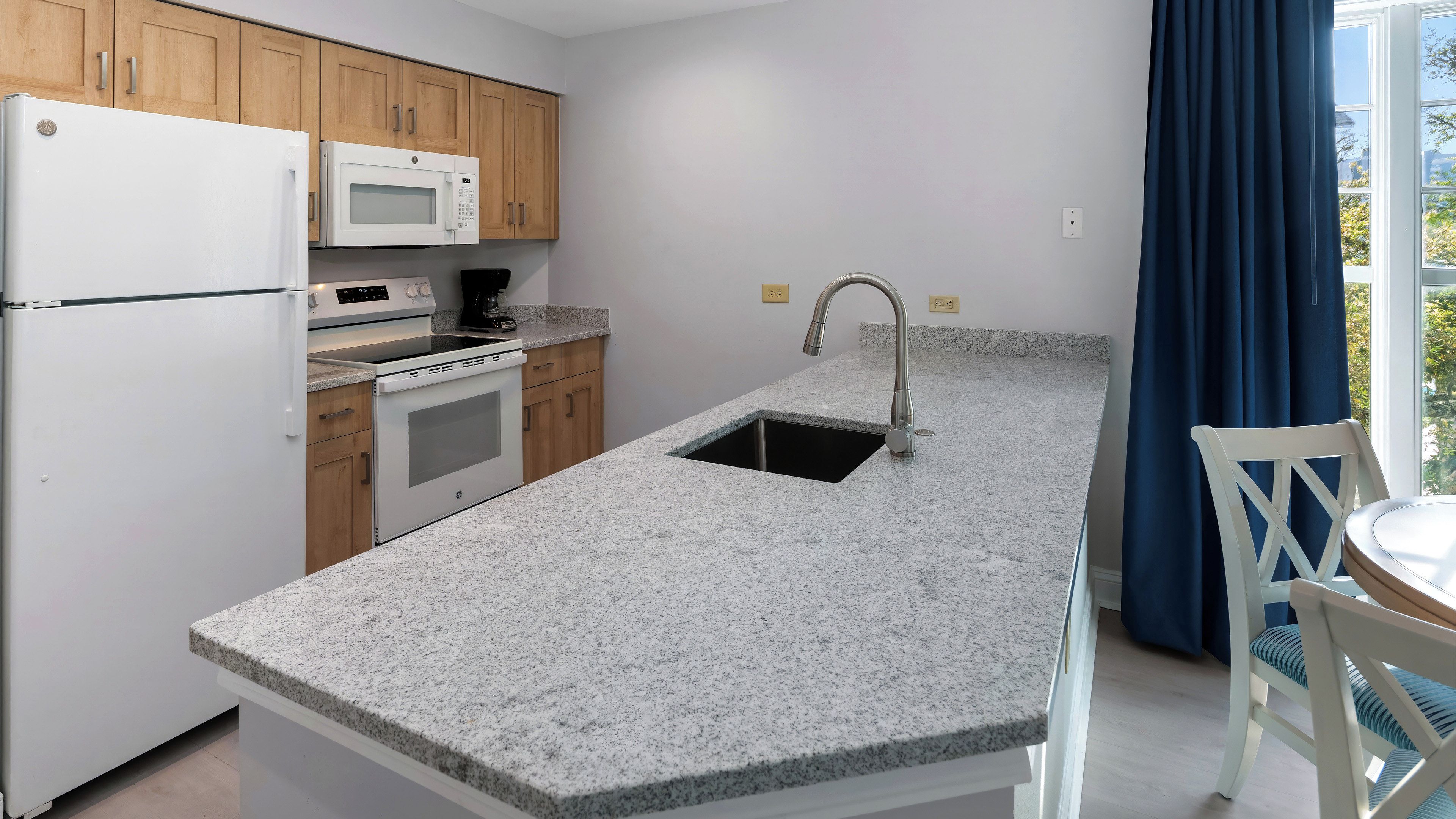 Una cocina con encimeras de granito, microondas integrado, estufa y pileta.