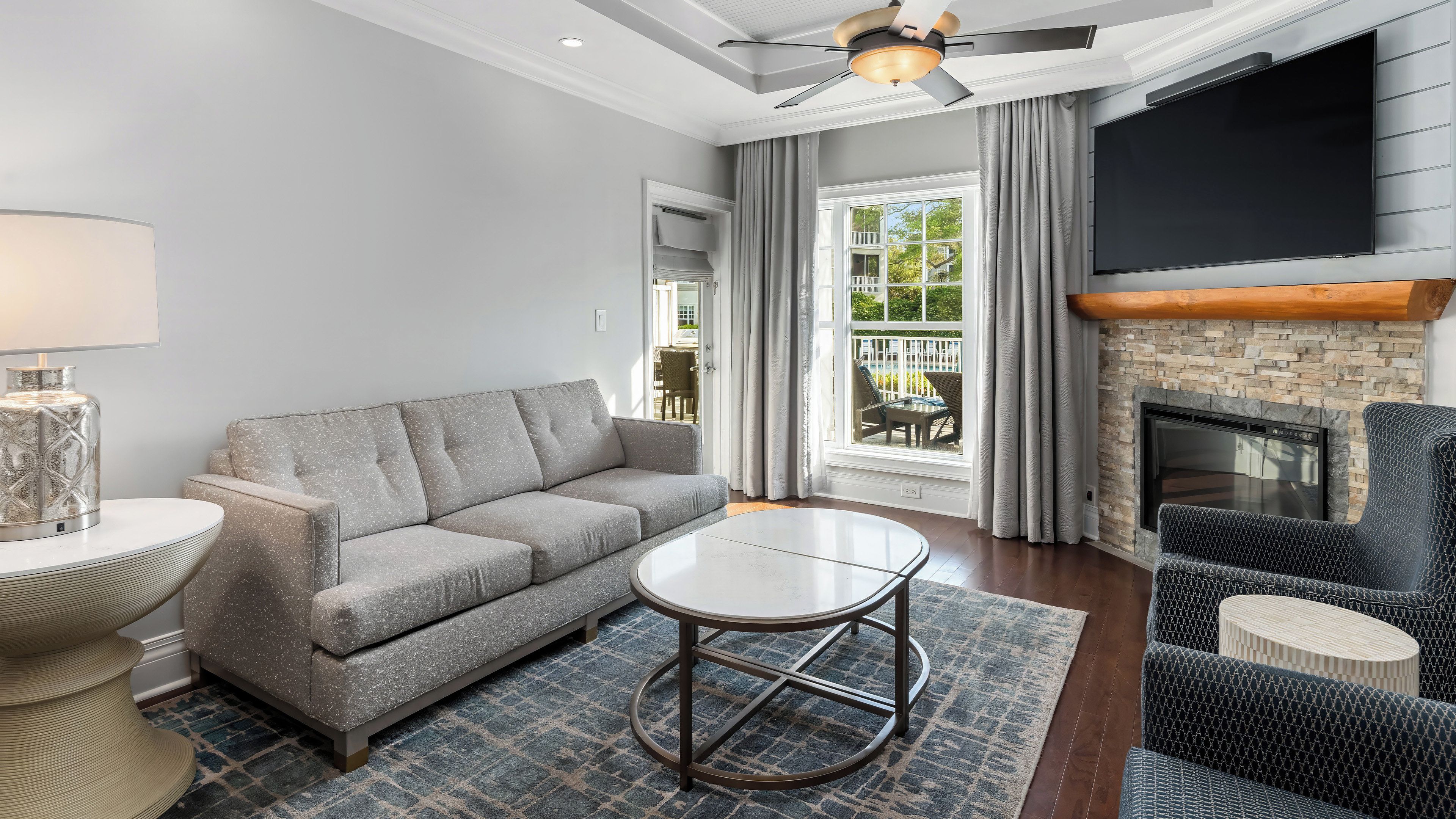 A modern living room with a grey sofa, a round coffee table, a fireplace, and a flat-screen TV mounted on the wall.