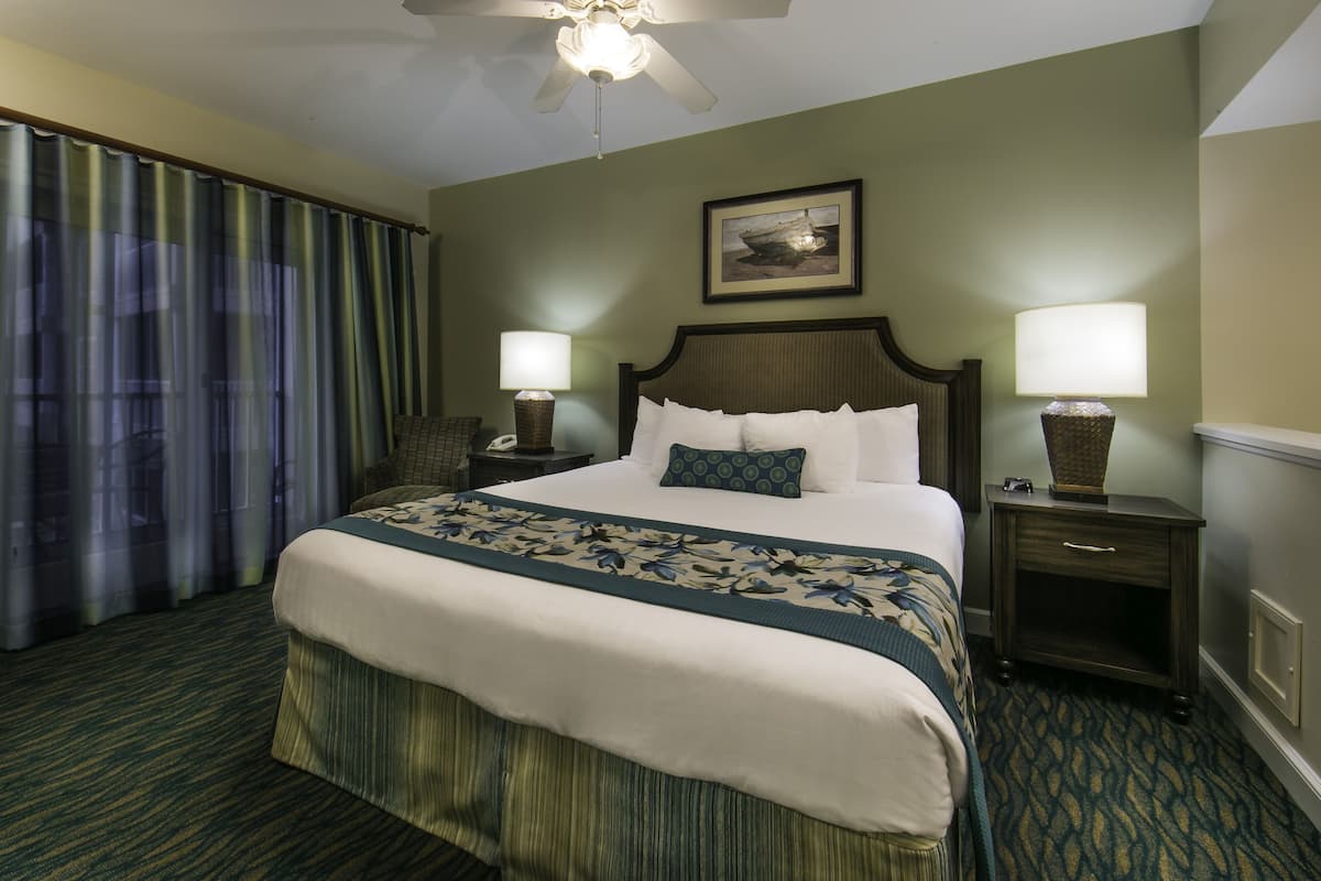 A hotel room with a large bed, two bedside tables with lamps, a ceiling fan, and a window with curtains.