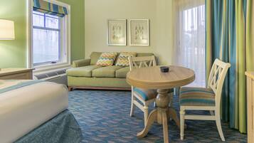 A hotel room with a bed, a green sofa, a dining table with chairs, and two framed pictures on the wall.