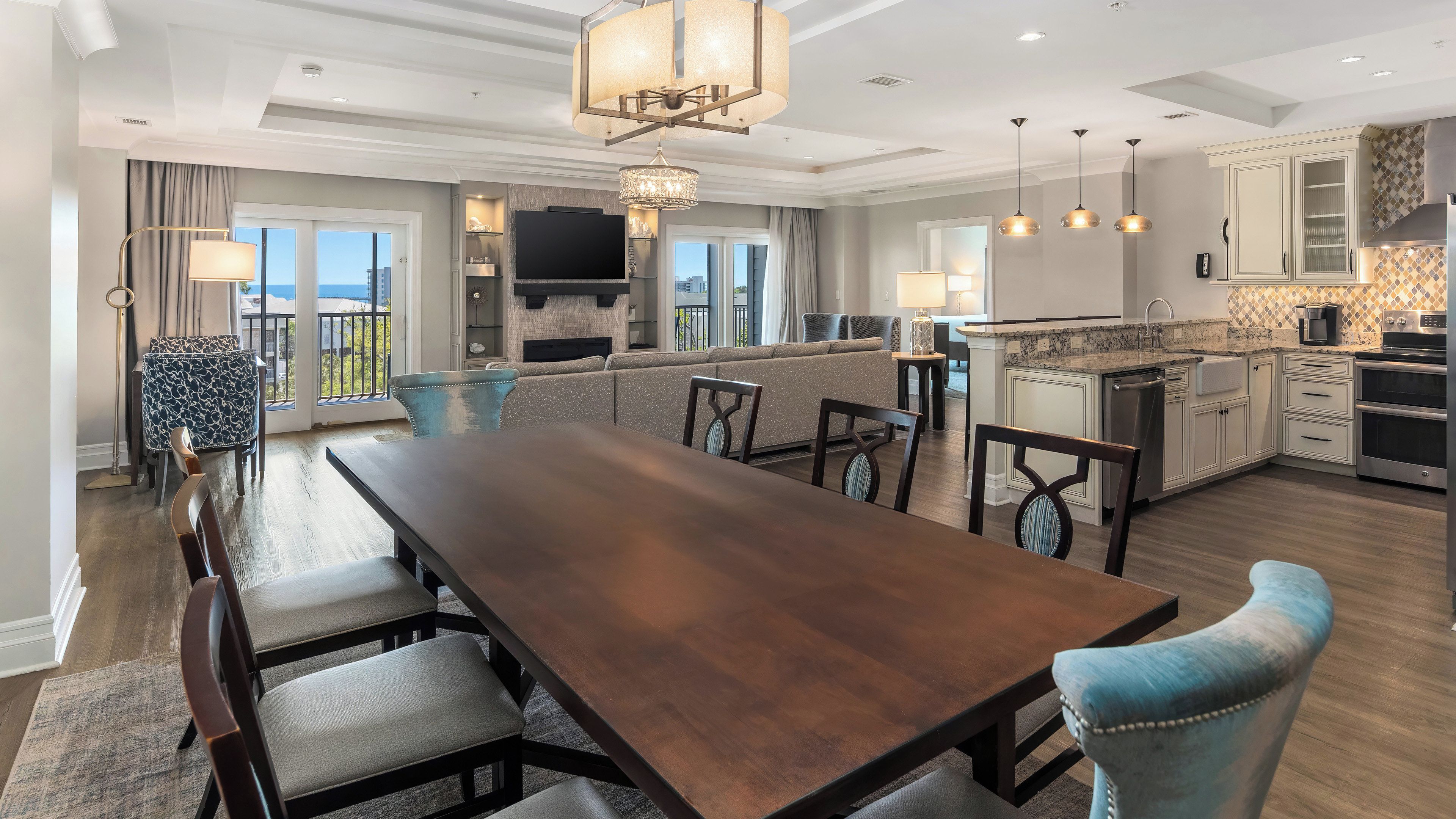Un comedor amplio con una larga mesa de madera y sillas, una cocina con electrodomésticos modernos, y un balcón con vistas.
