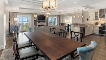 Un comedor amplio con una larga mesa de madera y sillas, una cocina con electrodomésticos modernos, y un balcón con vistas.