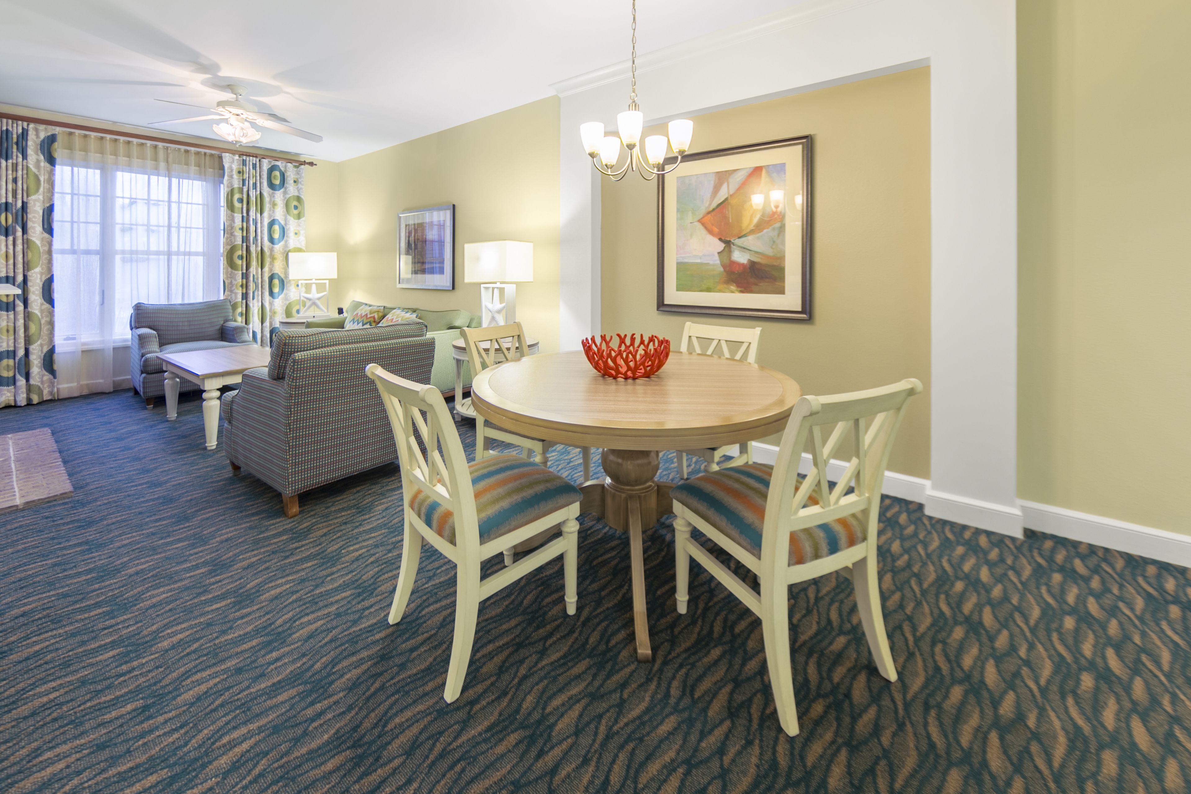 A hotel room with a dining table, chairs, a sofa, and a ceiling fan.