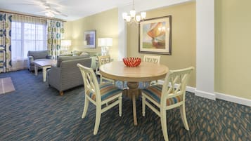 A hotel room with a dining table, chairs, a sofa, and a ceiling fan.