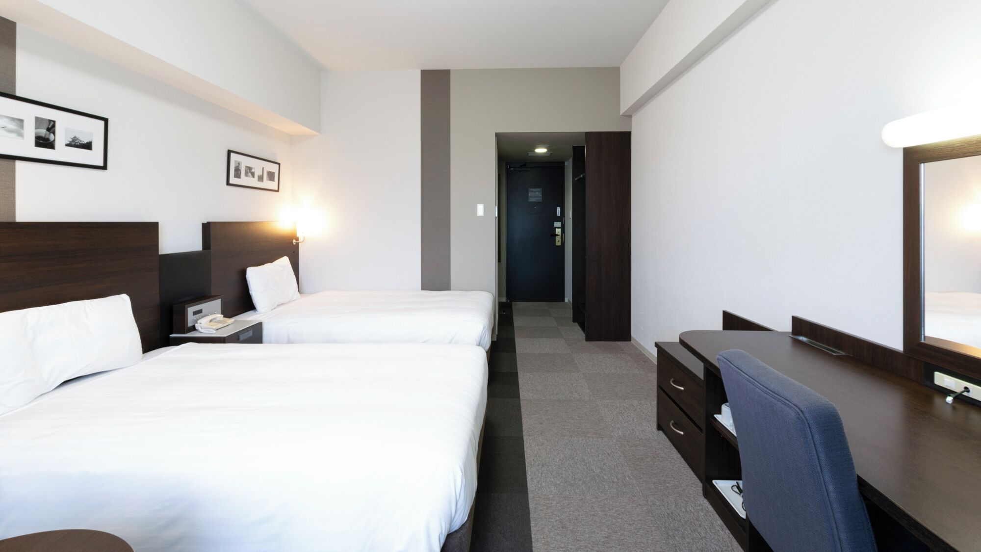Ein Hotelzimmer mit zwei Betten, einem Schreibtisch, einem Stuhl, einem Telefon und einem Spiegel.