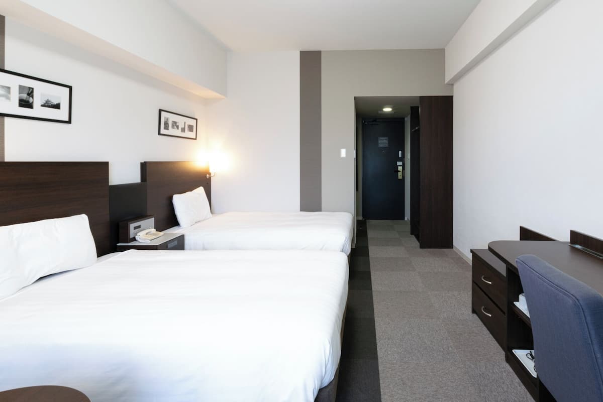 A hotel room with two beds, a desk, a chair, a phone, and a mirror.