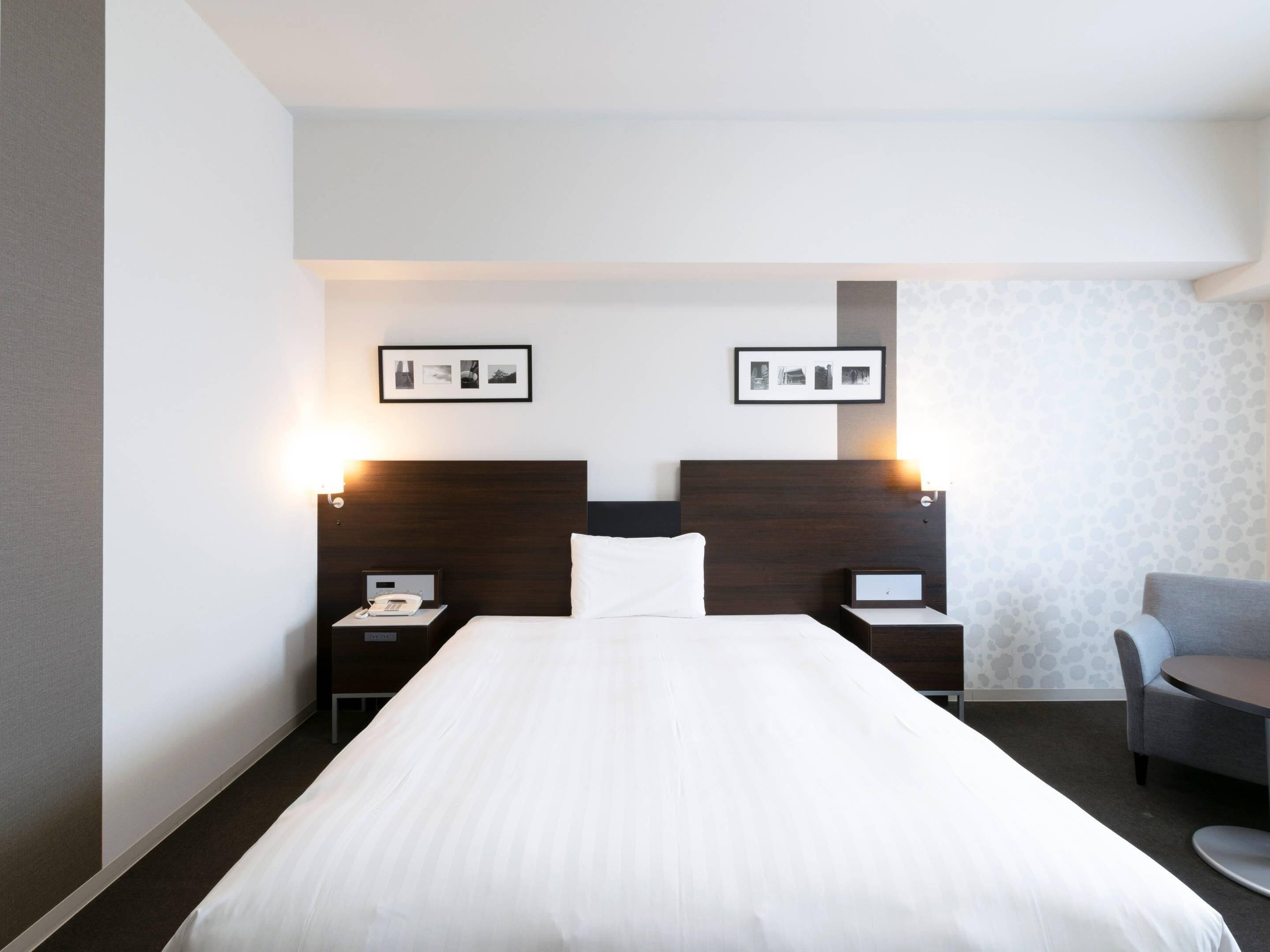 Une chambre d’hôtel avec un grand lit, deux tables de chevet avec des lampes, une chaise et des tableaux encadrés au mur.