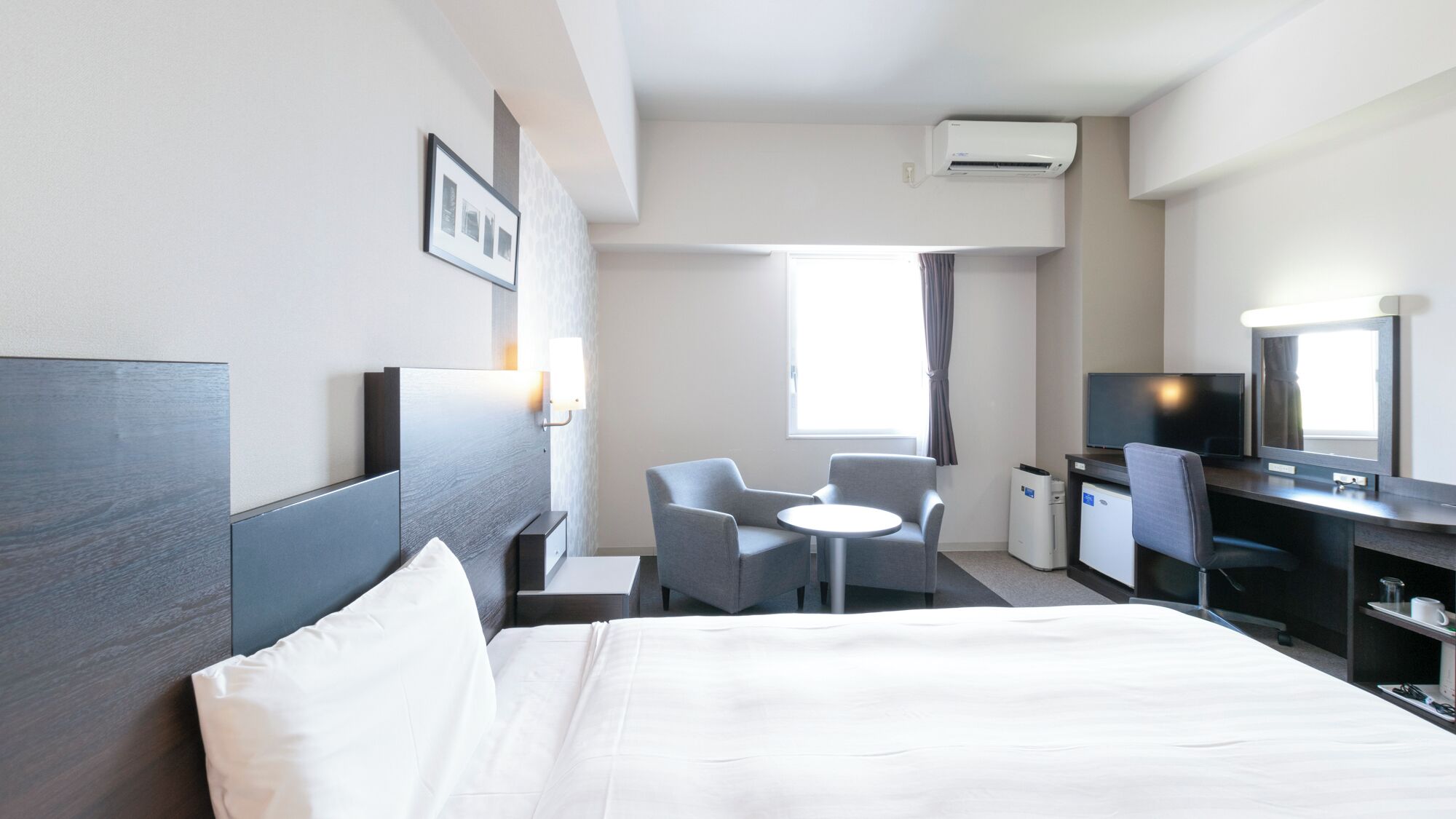 Ein Hotelzimmer mit einem Bett, einem Schreibtisch, einem Sessel, einem Fernseher und einer Klimaanlage.