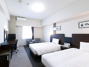 Une chambre d’hôtel avec deux lits, un bureau, une chaise, une télévision et une fenêtre avec des rideaux.